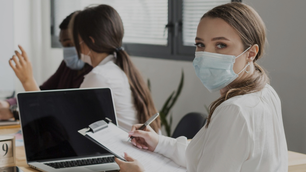 Mulher trabalhando no escritório durante a pandemia com máscara. Imagem representa a gestão médica durante a pandemia.