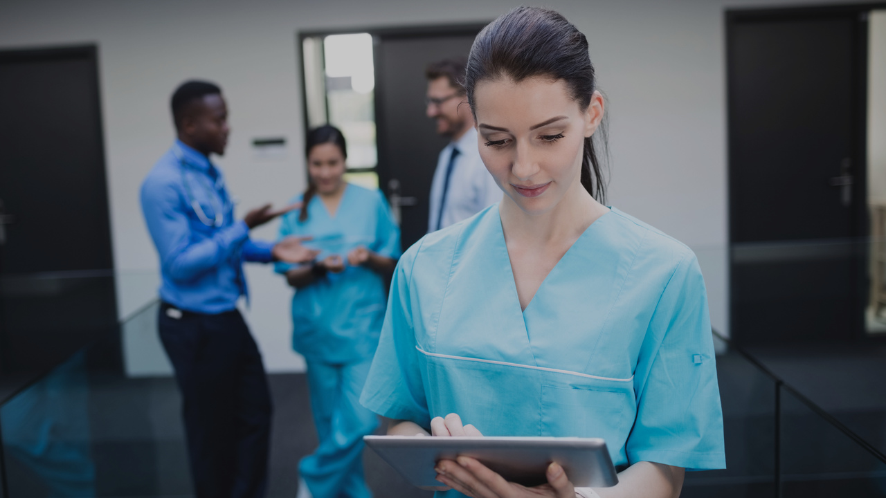 Médica segurando tablet e equipe conversando atrás dela. Imagem representa que o time pretende modernizar o consultório.