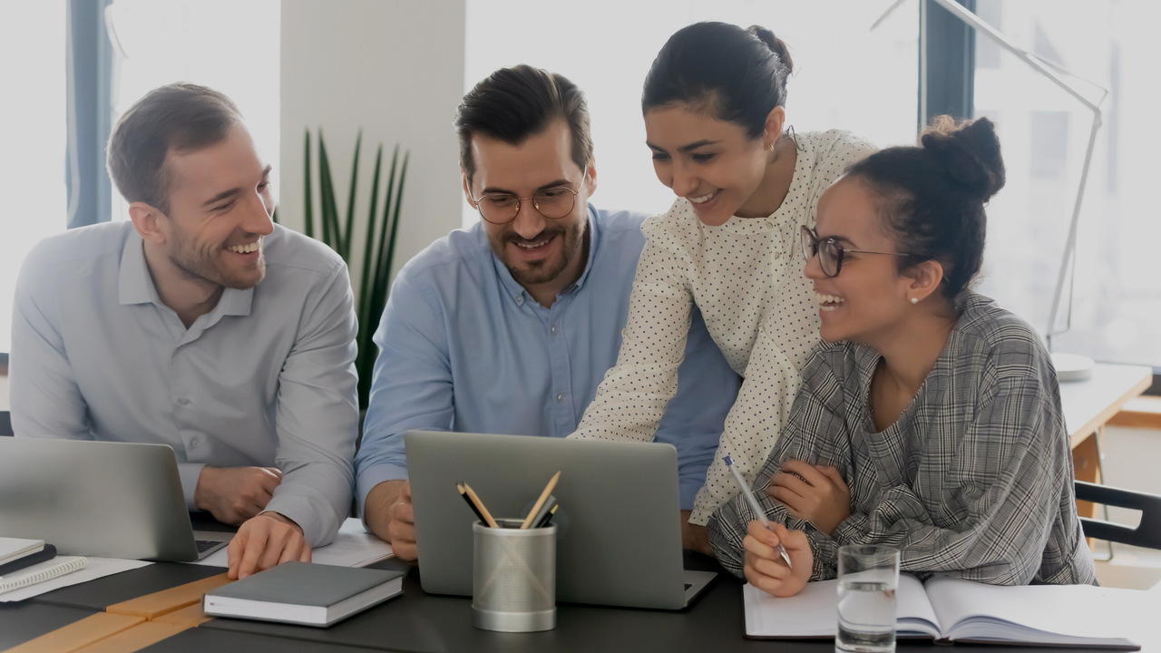 Quatro profissionais sorrindo em frente ao computador. Imagem simboliza que os profissionais estão controlando as glosas médicas.