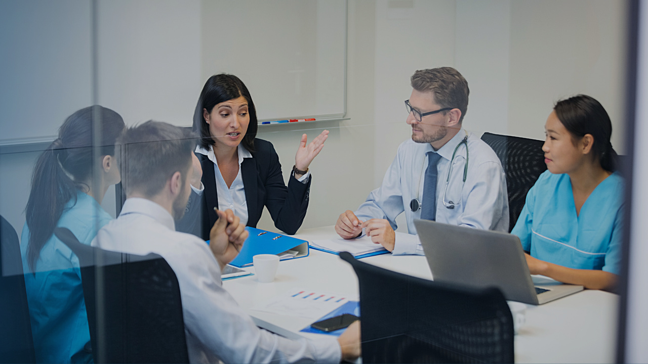 Profissionais de saúde e administrativos conversando. Imagem simboliza a discussão sobre os desafios atuais das operadoras de saúde.