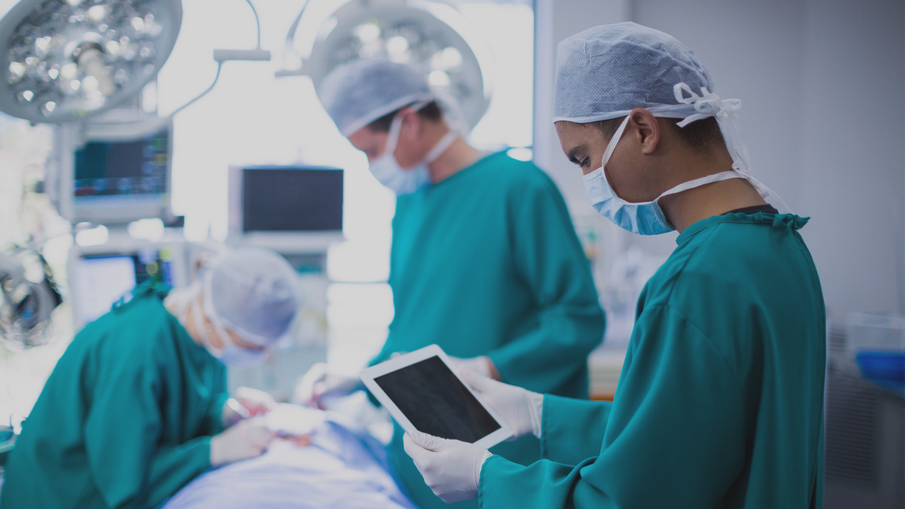 Cirurgião usando tablet digital na sala de operações. Imagem simboliza a gestão de equipamentos hospitalares.