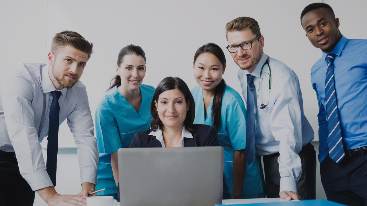 Equipe médica e administrativa em frente a um notebook. Imagem simboliza que estão verificando os benefícios do Validador TISS.