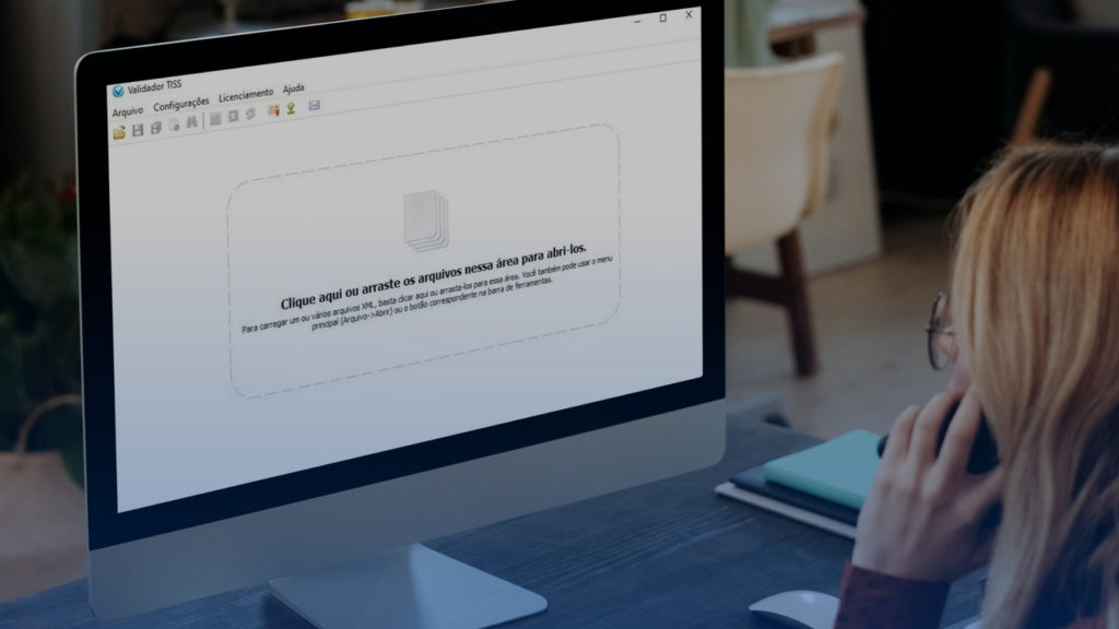 Mulher em frente ao computador, usando o Validador TISS. Imagem simboliza que ela está fazendo a correção de valores no sistema.