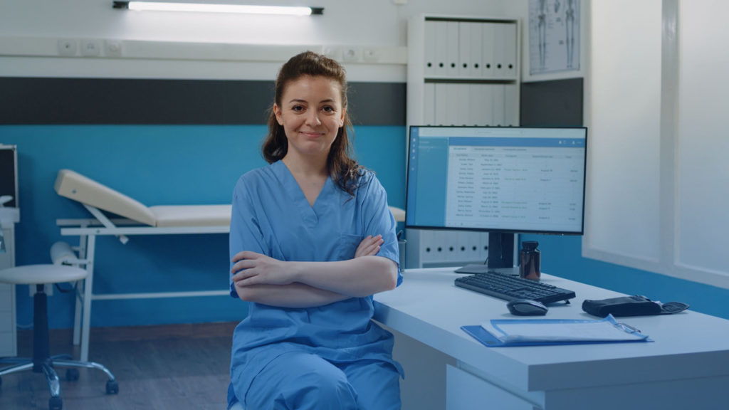 Mulher sentada em frente ao computador no consultório. Imagem representa profissional que ao contratar um software para a clínica, faz uso das funcionalidades do sistema.