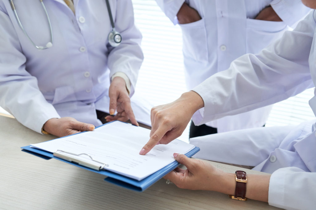 3 pessoas conversando e apontando para uma prancheta. A imagem representa os profissionais de faturamento hospitalar avaliando as causas das glosas hospitalares.